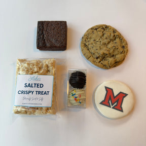 A flat-lay arrangement of five custom baked treats on a white background: a square brownie, a chocolate chip cookie, a packaged rice crispy treat labeled 'Salted Crispy Treat', a small packaged chocolate-covered treat, and a round white cookie with a red and black letter 'M'.